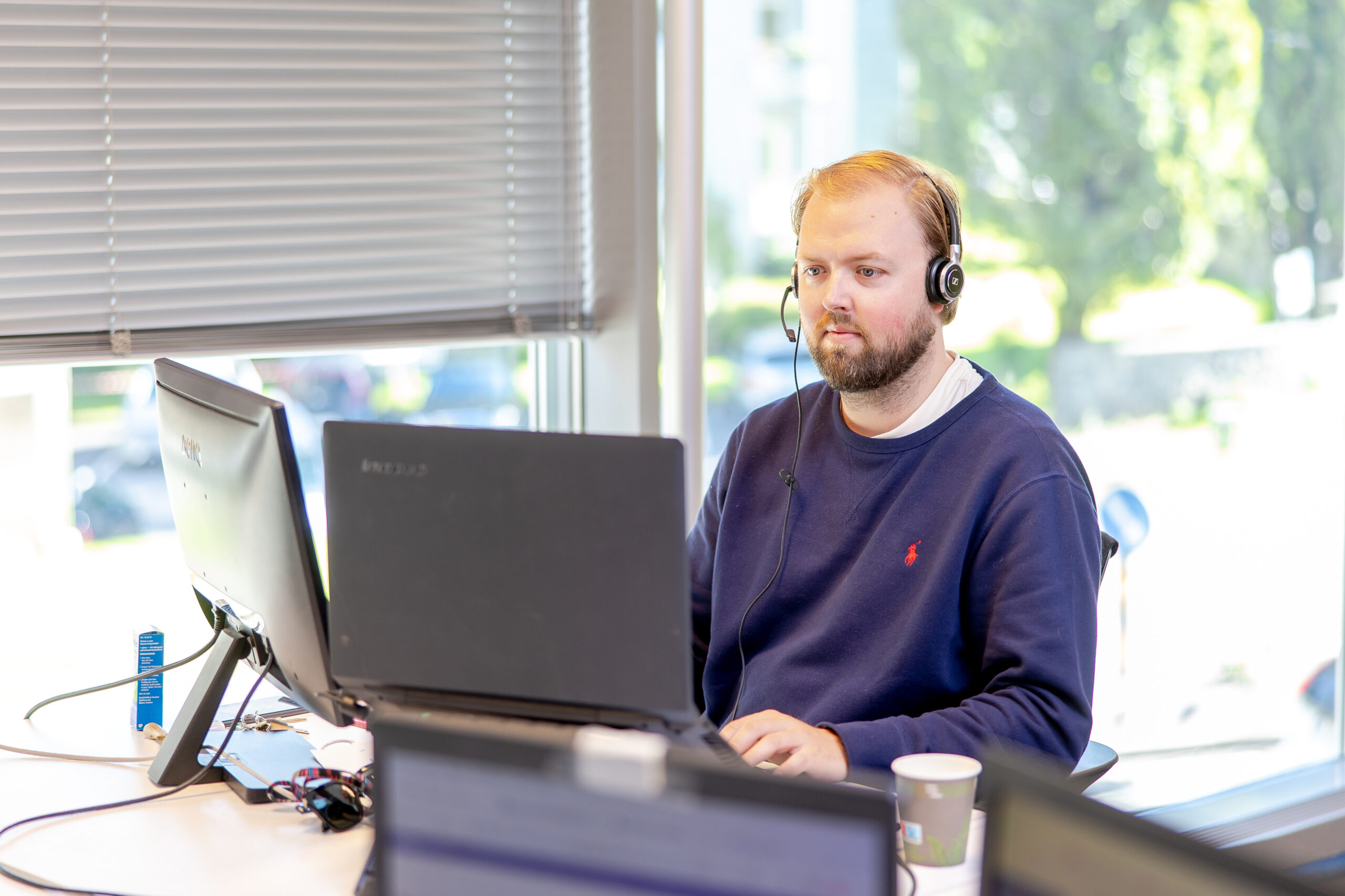 Ansatt med headset som jobber ved kontorpult foran laptop og skjerm